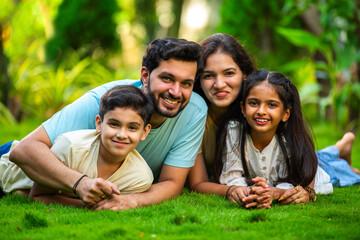 Happy Indian family of four sitting in park, embracing and smiling at camera, enjoying quality time