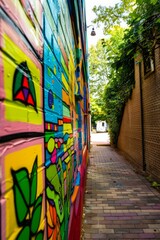 Wall Mural - Colorful graffiti wall in a narrow alleyway with a brick wall on the opposite side.