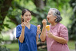 © kamonrat - Elderly woman and young nurse enjoy ice cream together in a relaxing outdoor park environment