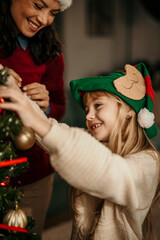 Happy mother and little daughter decorating christmas tree at home. family, winter holidays and people concept