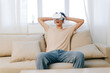 © SHOTPRIME STUDIO - Young man experiencing virtual reality entertainment at home, seated comfortably on a sofa, immersed in gaming with excitement Soft, bright interior lighting enhances the atmosphere