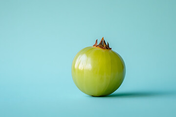 Canvas Print - A single green tomato on a light blue background, emphasizing its color and shape.