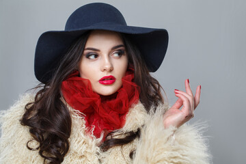 Cute woman with red lips make-up and long wavy hair wearing blue hat against dark studio wall background