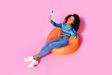 Poster - Full size photo of pretty young girl sit orange beanbag selfie photo talk wear trendy blue outfit isolated on pink color background