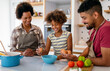 © NDABCREATIVITY - Happy african american family preparing healthy food in kitchen, having fun together on weekend