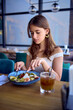 © Victoria Antre - A 16-year-old teenage girl in old money style clothes is eating salad with coffee in a fancy restaurant