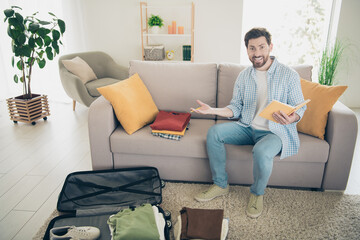 Sticker - Photo of bearded confused mature age man sitting indoors living room with huge couch dont know what need packing clothes inside suitcase