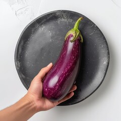 Wall Mural - Hand holding a ripe eggplant over a black plate.