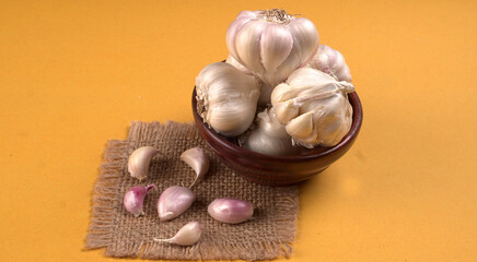 Organic Garlic. Fresh Garlic Cloves and Garlic bulb in wooden basket on yellow background with Pile of garlic or spice. Concept of spices for healthy cooking.