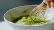 © AUNTYANN STUDIO - A hand whisking matcha green tea powder in a bowl using a traditional bamboo chasen, emphasizing a step in preparing a matcha beverage.