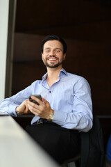 Wall Mural - A man is sitting at a table with a cell phone in his hand. He is smiling and he is happy