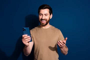 Wall Mural - Photo portrait of young handsome guy brunet hair model in beige t shirt phone video call isolated on dark blue color background