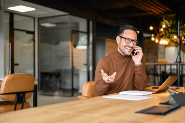 Wall Mural - handsome manager discussing over phone call while working on project over laptop at his workplace