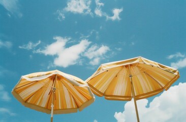 Two yellow beach umbrellas against a bright blue sky with fluffy white clouds A cheerful summer atmosphere is evoked