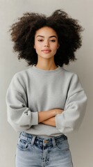 Wall Mural - A young woman with natural, curly hair wearing a casual, oversized sweater and jeans, standing confidently in a minimalist urban setting, highlighting effortless style and comfort