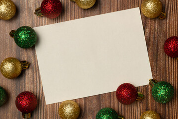 Empty white paper with Christmas balls on wooden background from above. Flat lay, top view. Space for text.