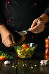 Wall Mural - A cook at the kitchen table prepares a vegetable dinner. The chef adds paprika to the vegetable salad. Service concept for a restaurant or hotel