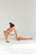 © yavdat - A woman in beige workout attire engages in a deep stretch yoga pose, her body extended forward on a seamless white background. This image captures the essence of mindfulness and physical fitness.