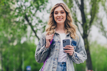 Poster - Photo of nice young woman hold smart phone backpack wear denim jacket walk city center outdoors