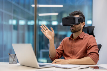 Young professional in modern office using virtual reality headset while interacting with laptop for innovative experience. Person explores new technology concepts, enhancing digital interaction