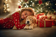 © Victor - Little girl posing with her dog next to the Christmas tree full of presents on Christmas day