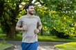 © Tetiana - Smiling man jogging in the park with earphones enjoying morning exercise in nature.