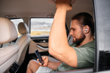 Wall Mural - Man using smartphone in the back seat of a car, relaxed lifestyle setting