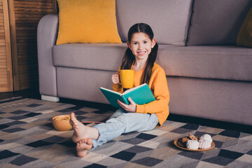 Poster - Full length photo of little girl sit floor read book drink tea snacks dressed orange garment spend pastime spacious house indoors room