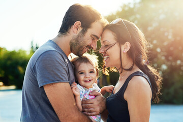 Wall Mural - Happy, love and parents with baby in park for bonding, loving relationship and relax together outdoors. Family, sunshine and mom, dad and child for embrace, affection and forehead touch on weekend