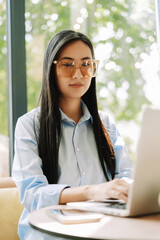 Young asian manager woman wearing stylish eyeglasses working on laptop computer in cafe