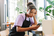 © Maria Vitkovska - African American waitress feeling stressed while checking smartphone in a cafe