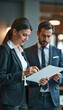 © Juan Mari - A female executive reviews important documents with a male colleague in a modern office setting. Perfect for corporate presentations, business articles, and marketing materials