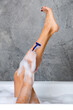 © Nobilior - Woman shaving legs with razor in bathtub on gray wall background.