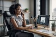 © polack - In the office, an attractive happy African American woman sits in a chair, smiling and using a mobile phone