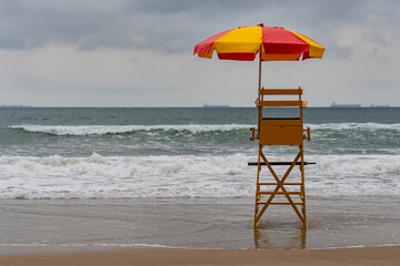 Wall Mural - An empty lifeguard chair in front of a tourist beach that has strong waves. Tombo beach, Guaruja - SP- Brazil.