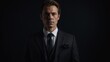 © JohnDesignHub - Serious young man in black suit posed against dark backdrop backdrop