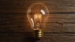 © JohnDesignHub - Classic incandescent light bulb with visible filament on wooden wall.