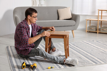 Canvas Print - Man using tape measure while repairing wooden stool indoors