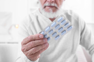 Poster - Senior man holding blister with pills at home, closeup