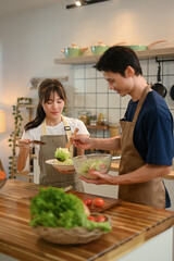 Wall Mural - Young couple wearing aprons enjoying their cooking time in a modern kitchen. Healthy and nutritious lifestyle concept