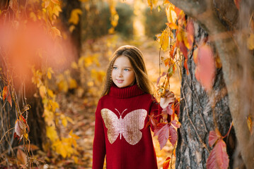 Wall Mural - Cute baby girl with long hair in autumn in the park is smiling and enjoying a sunny day and good weather. Autumn walks and leisure for preschoolers