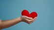 © Harshana - Two hands gently cradle a bright red heart against a soft blue background, creating a striking contrast that symbolizes love, care, and tranquility. The image conveys warmth and affection, reflecting