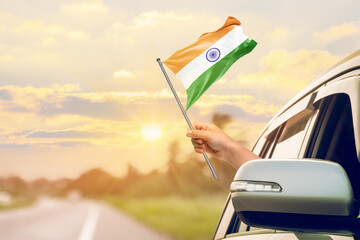 Waving the India flag against the sunrise or sunset from a car driving along a country road. Holding the India flag, traveling by car, on a weekend trip.