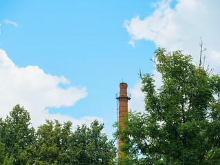 A tall brick chimney is visible in the sky above a forest. The sky is clear and blue, with a few clouds scattered throughout. The chimney is a prominent feature in the scene without a smoke