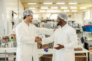 Wall Mural - Smiling multicultural manager shaking hands with new employee in food factory.