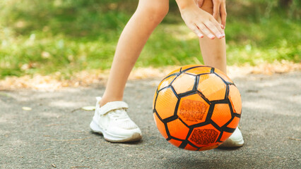 feet in sneakers and soccer ball on road in sun. children play football. activity sport in summer.