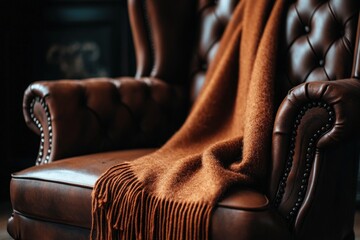 A rust-colored fuzzy blanket draped over a luxurious, vintage leather armchair. The armchair features button-tufted details and creates a cozy, rustic atmosphere in the room.