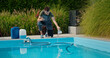 © StockMediaSeller - Pool technician pouring liquid into the pool while using a tablet, with chemical containers and greenery in the background.