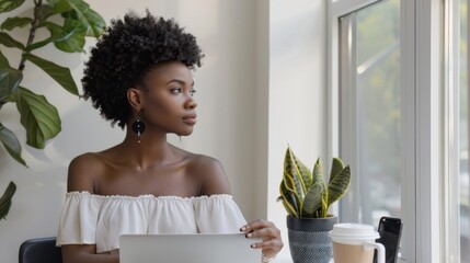 Wall Mural - A woman with curly hair is sitting at a table with a laptop and a cup of coffee