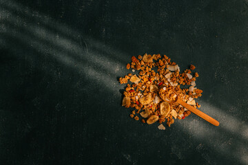 Overhead view of a wooden spoon with scattered granola, dried banana chips, and coconut flakes on a dark textured background